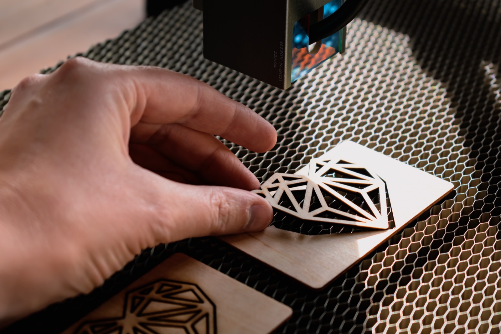 A hand lifting a laser-cut wooden heart keepsake from the engraving bed